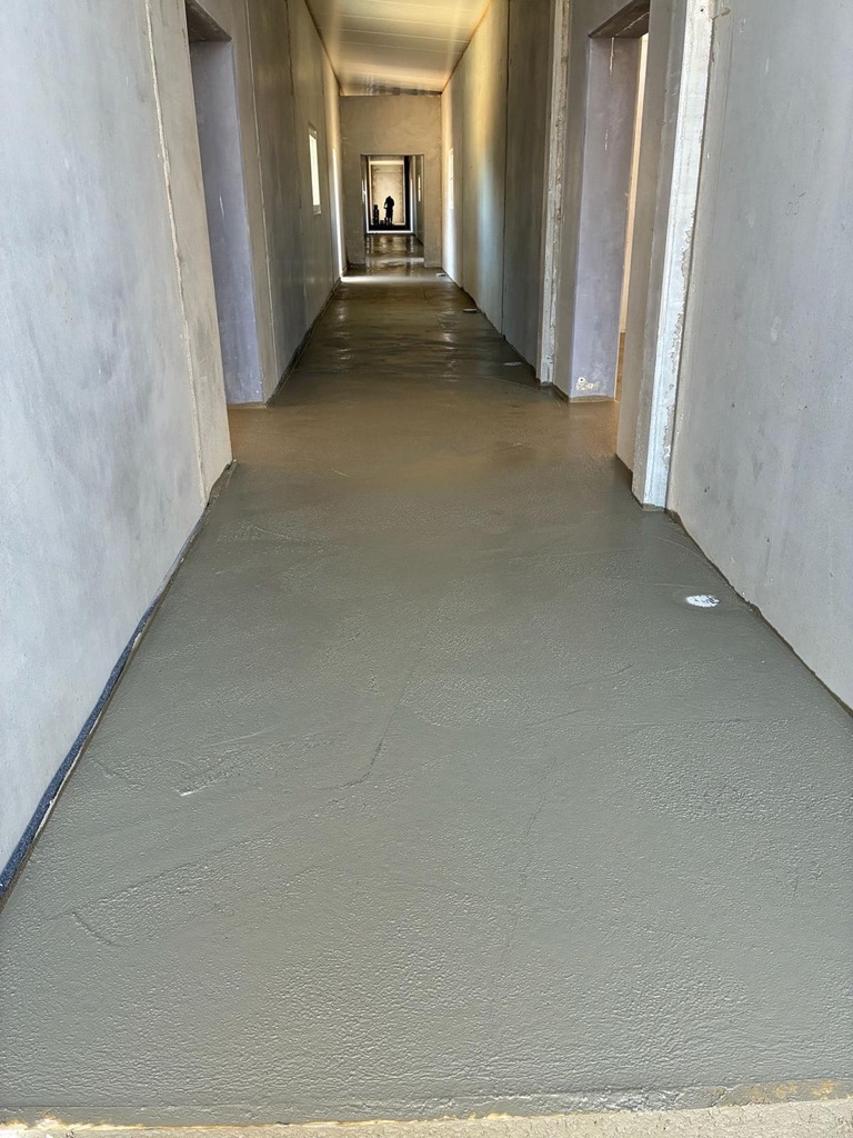 Innenkorridor im Rohbau mit frisch verputztem Betonboden und Person im Hintergrund
