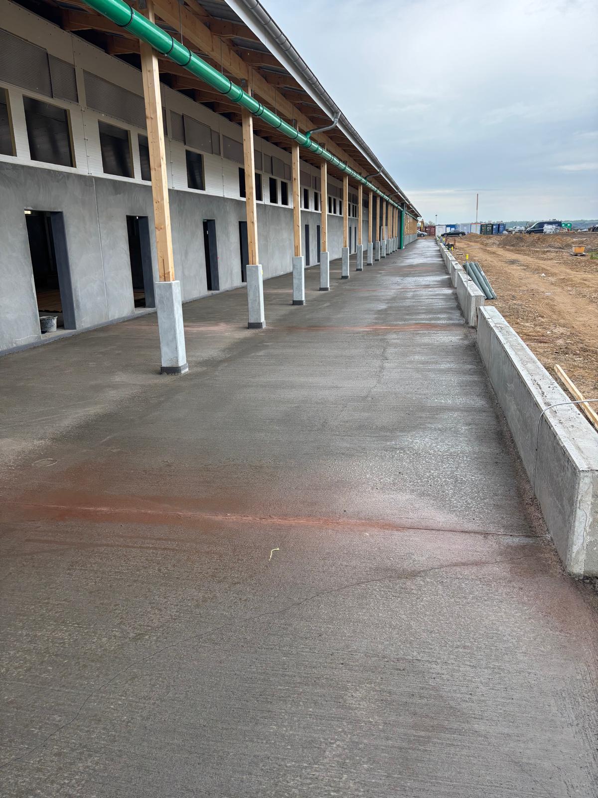 Überdachter Laufgang mit grünen Fallrohren entlang der Stallhalle