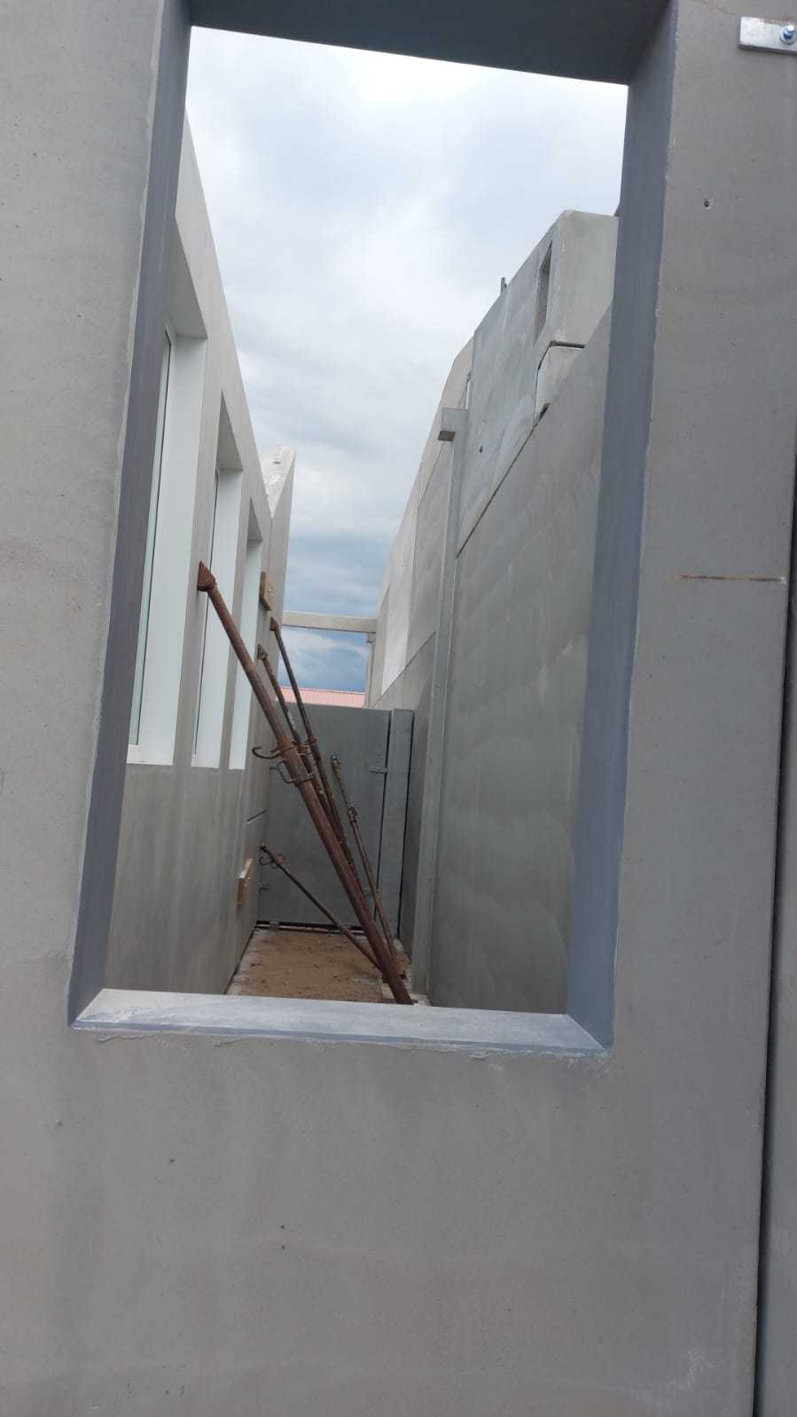 Blick durch eine Fensteröffnung auf montierte, abgestrebte Betonwandelemente